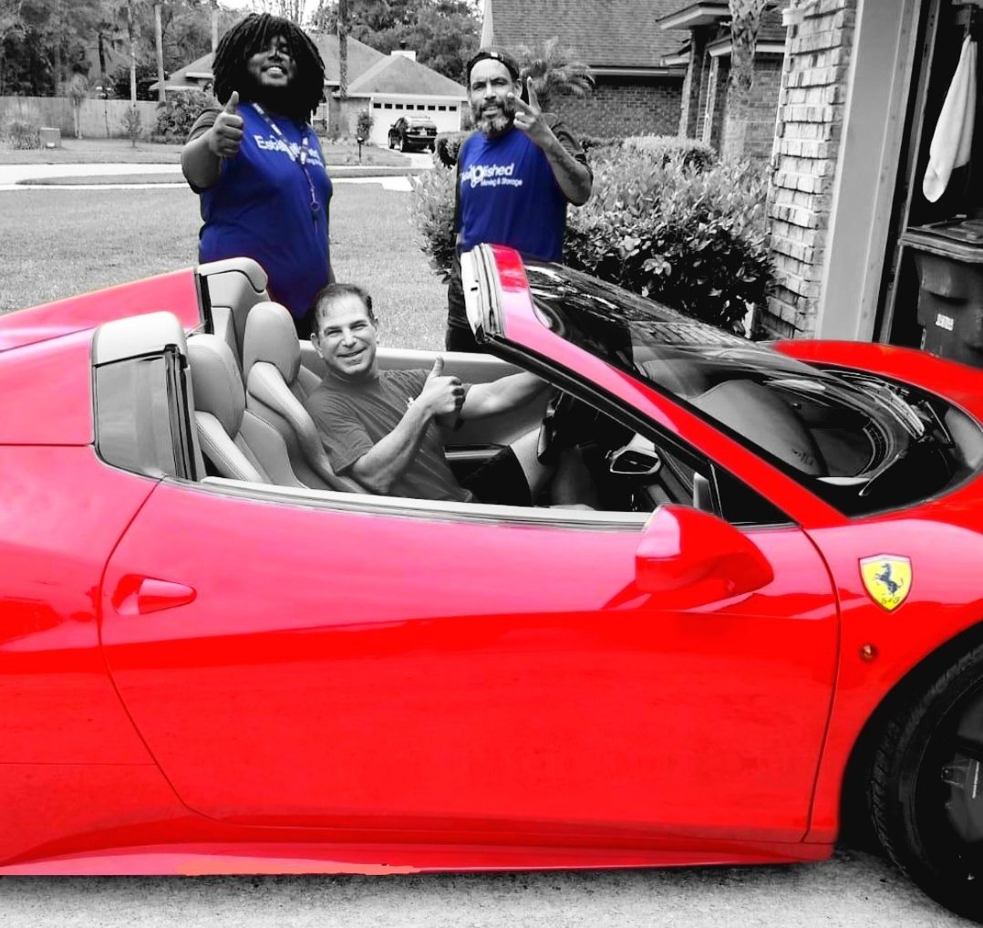 Two established moving employees give a thumbs up with a customer in his red car
