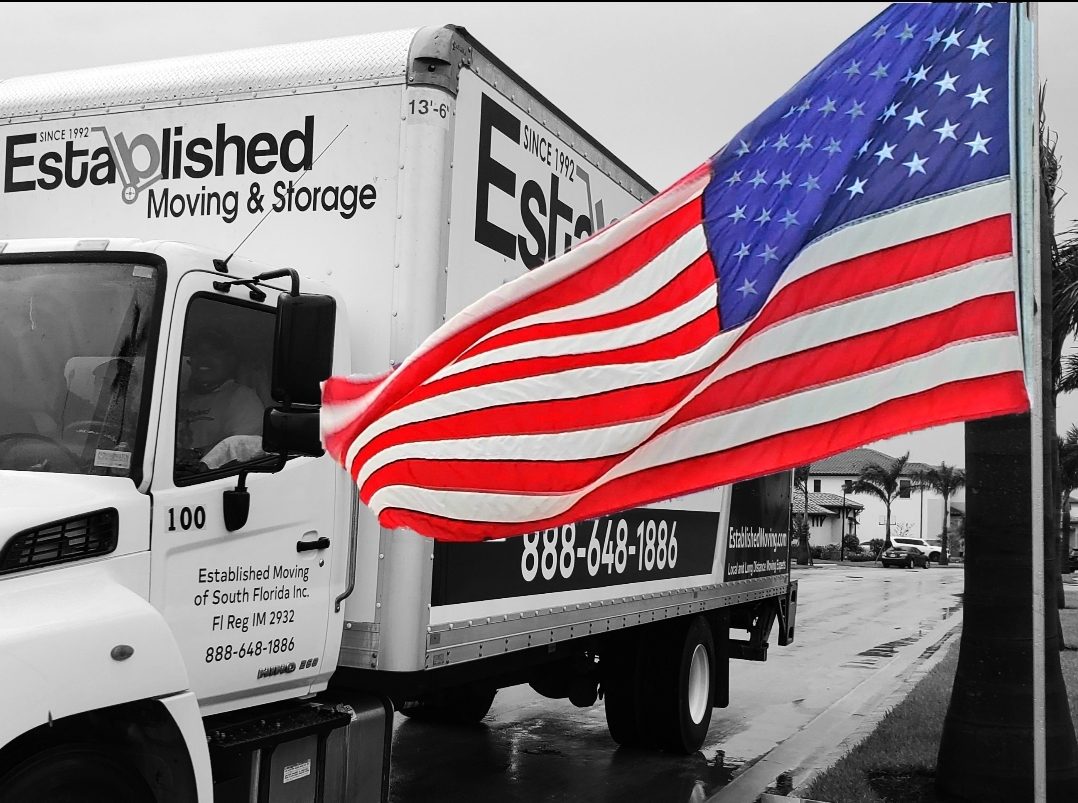 an american flag waves in front of an established moving & storage truck