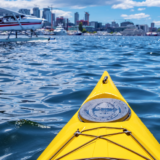 a person on a kayak taking a picture of an aquatic aero plane with the Seattle skyline in the background