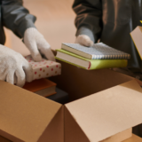 Two movers packing books into a box.