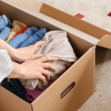 Hands of a woman packing clothes into a cardboard box.